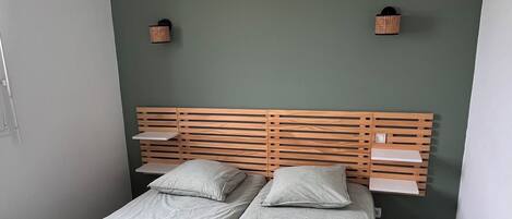 A double bed with a wooden headboard, two bedside tables, and a green wall.