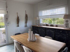Une cuisine avec une table en bois, deux décorations murales en forme de poisson, une fenêtre donnant sur un paysage agréable et un meuble avec une lampe.