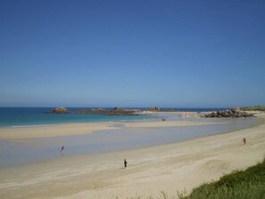 A wide sandy beach with calm waters, a few rocks, and a clear sky.