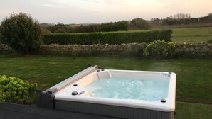 A hot tub on a deck with a stone wall and greenery in the background. - A haven of peace with Spa at 2 steps from the beach (Cléder)