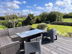 Une terrasse extérieure aménagée avec des meubles en osier et une table, entourée d’un jardin bien entretenu et d’un mur en pierre.