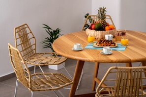 A round wooden table with a wicker chair arrangement, a fruit basket, and breakfast items including toast and orange juice. - Santorini Caves (Santorini)