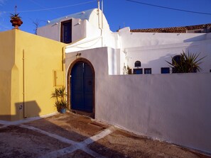 A building with a blue door and a yellow wall, featuring a small garden area with potted plants. - Santorini Caves (Santorini)