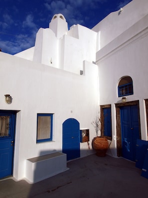 A white building with blue doors and windows, a large pot, and a small tree. - Santorini Caves (Santorini)