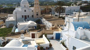 Un edificio blanco con un campanario, rodeado de construcciones más pequeñas y plantas en macetas.