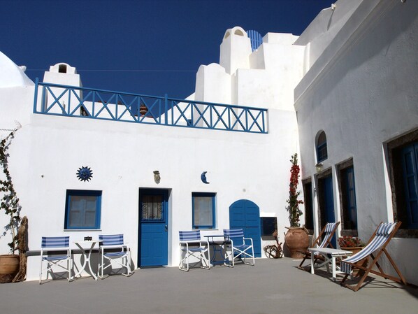 A white building with blue doors and windows, a balcony with blue railings, and outdoor seating with chairs and tables. - Santorini Caves (Santorini)