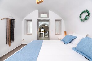 A bedroom with a large bed, a wardrobe, and a view into another room. - Santorini Caves (Santorini)
