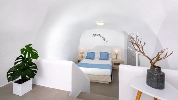 Un dormitorio moderno con decoración en blanco, una cama, mesitas de noche y una planta en maceta.