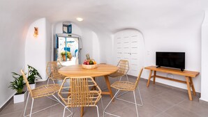 Una sala de estar moderna con una mesa redonda de madera, cuatro sillas de mimbre, un televisor sobre un mueble de madera y una planta en maceta.