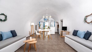 Una sala moderna con sofá, mesa de comedor y sillas, una zona de cocina al fondo y un televisor sobre un mueble.