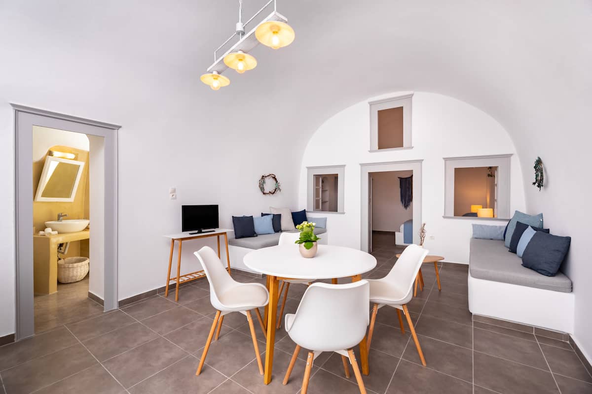 A modern living room with a white sofa, a dining table with chairs, a TV, and a small plant.