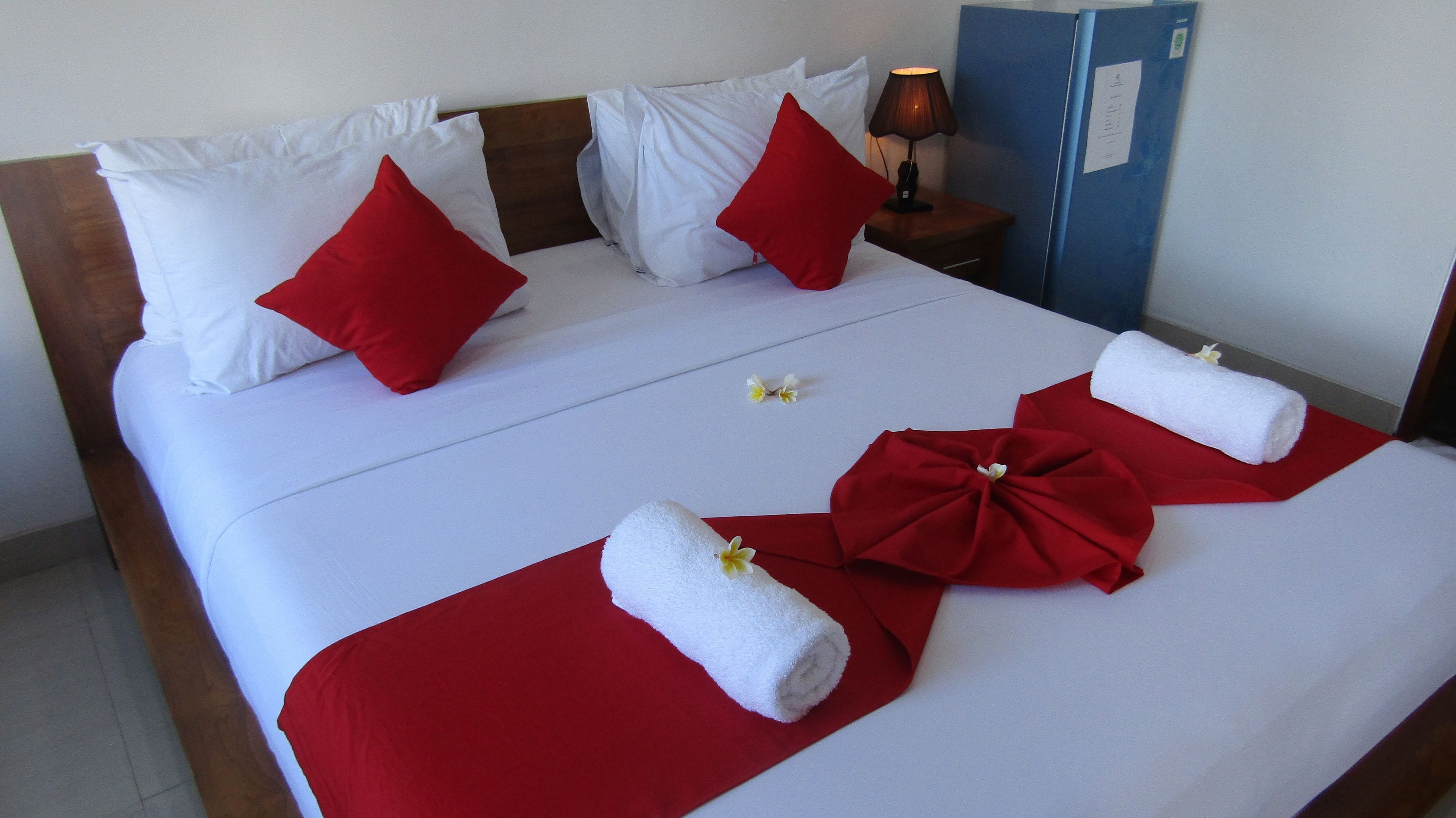 A neatly made bed with white and red bedding, a wooden headboard, a nightstand with a lamp, and a blue cabinet.
