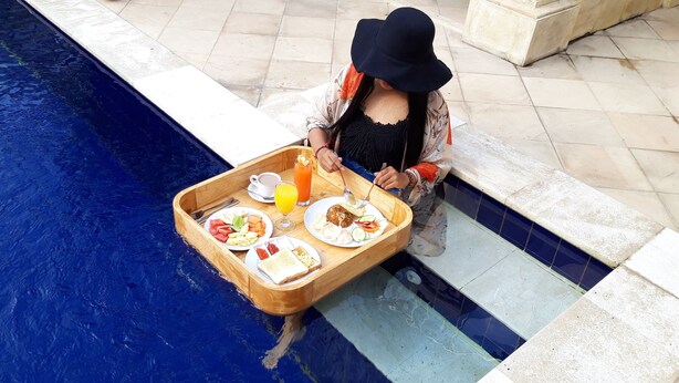 A dining table with breakfast items by a poolside. - Grand Raka Homestay (Buleleng)