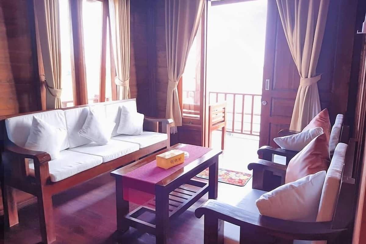 A cozy room with a wooden sofa, a wooden table, and a chair. There is a window with curtains, and a door leading outside.