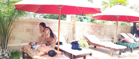 A spa area with massage tables, red umbrellas, and a stone wall.