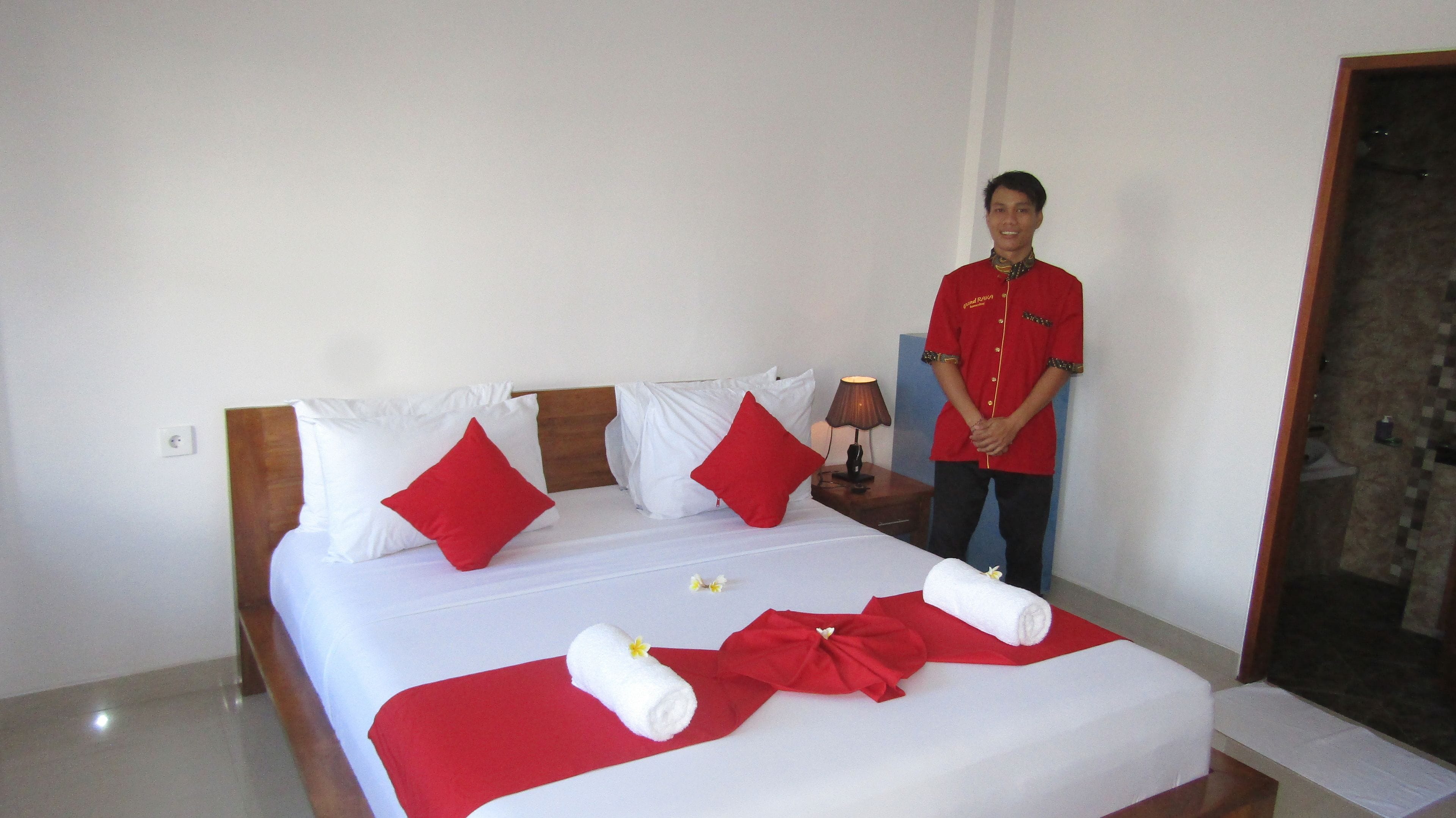 A hotel room with a neatly made bed, red and white pillows, and a red and white bedspread.