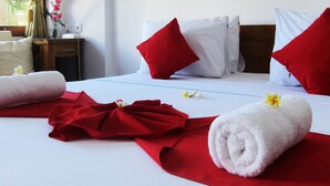 A hotel room with a neatly made bed, red towels, and white pillows. - Grand Raka Homestay (Buleleng)