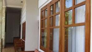 A hallway with wooden benches and large windows with curtains. - Grand Raka Homestay (Buleleng)