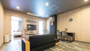 A modern room with a sofa, a desk, and a chair. There is a bed in the background, and a window with curtains. - S-Dotonbori Hotel Namba (Osaka)