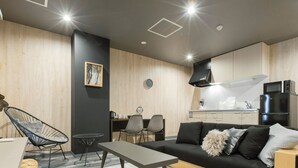 A modern living room with a black sofa, a dining table, and a kitchen area with a black refrigerator and microwave. - S-Dotonbori Hotel Namba (Osaka)