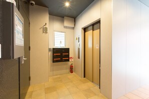A hallway with a fire extinguisher, an elevator, and a door with a sign. - S-Dotonbori Hotel Namba (Osaka)