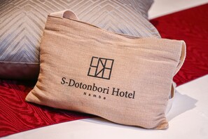 A beige pillow with the logo and name of S-Dotonbori Hotel Namba. - S-Dotonbori Hotel Namba (Osaka)