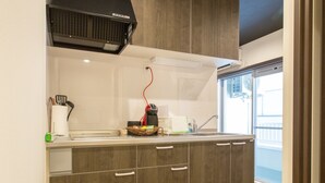 A modern kitchen with dark wood cabinets, a black range hood, and a window providing a view of the outside. - S-Dotonbori Hotel Namba (Osaka)