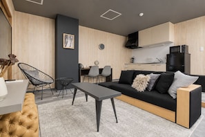 A modern living room with a black sofa, a coffee table, and a dining area with chairs.