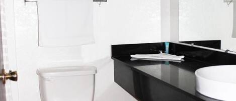 A bathroom with a white toilet, black countertop, and a framed picture on the wall.