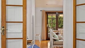 A room with a wooden floor, white walls, and a large window with curtains. There are two white chairs and a small table in the room. - Frangipani House (East Toowoomba)