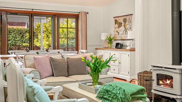 A cozy living room with a sofa, a fireplace, and a view of greenery outside. - Frangipani House (East Toowoomba)