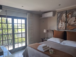 Habitación de hotel con un ventanal grande, cama con toallas ordenadas, mesita de noche con lámpara y aire acondicionado de pared.