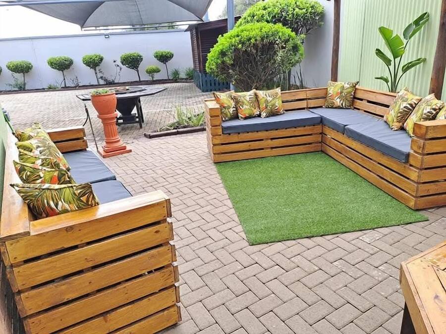 Un patio con un banco de madera, una mesa pequeña y una zona de césped artificial verde.