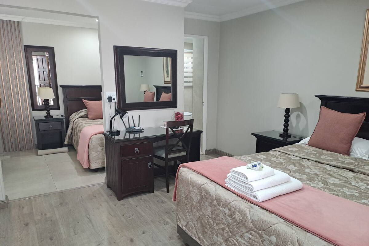 A hotel room with a bed, a desk with a mirror, a chair, and a nightstand.