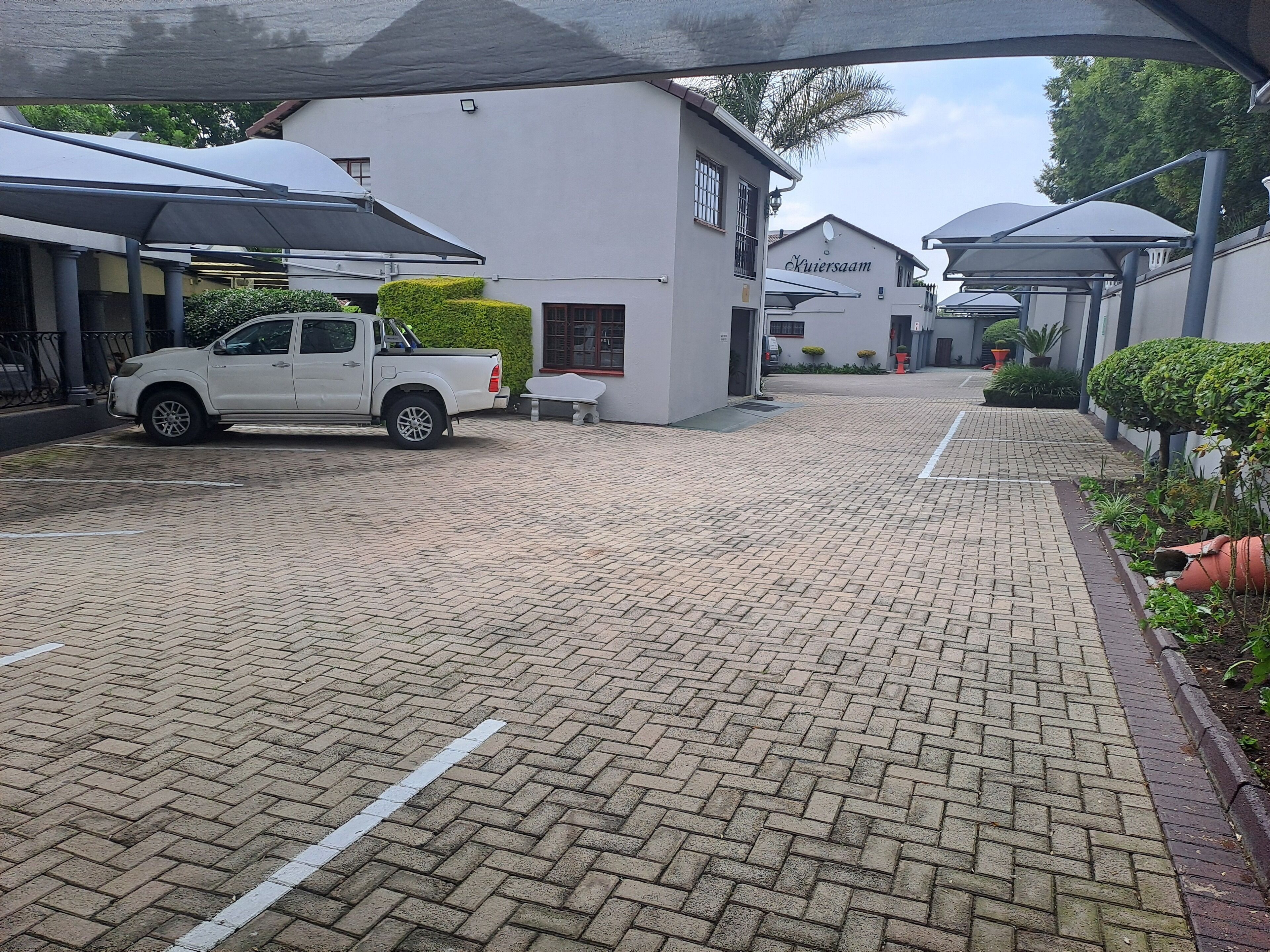 A white pickup truck parked in a paved driveway with a white building labeled "Kuizersam" in the background.