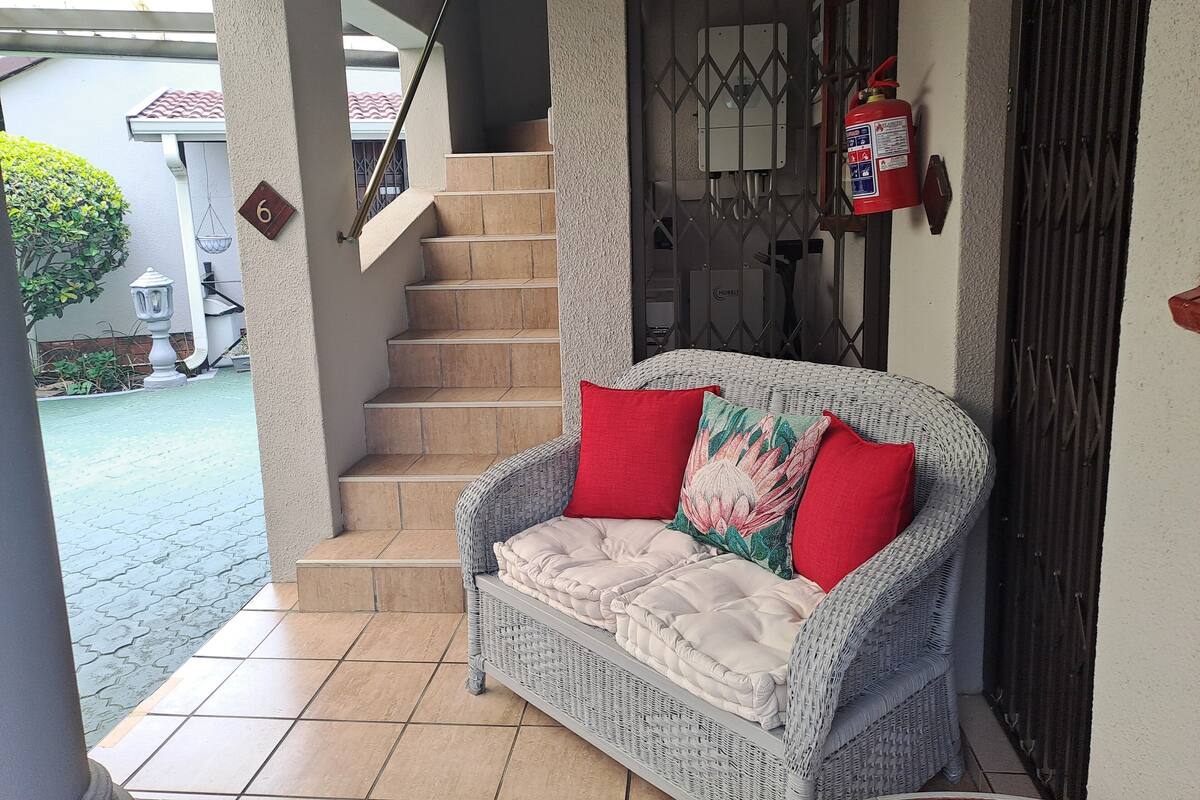 A wicker sofa with red cushions, a staircase, and a fire extinguisher on the wall.