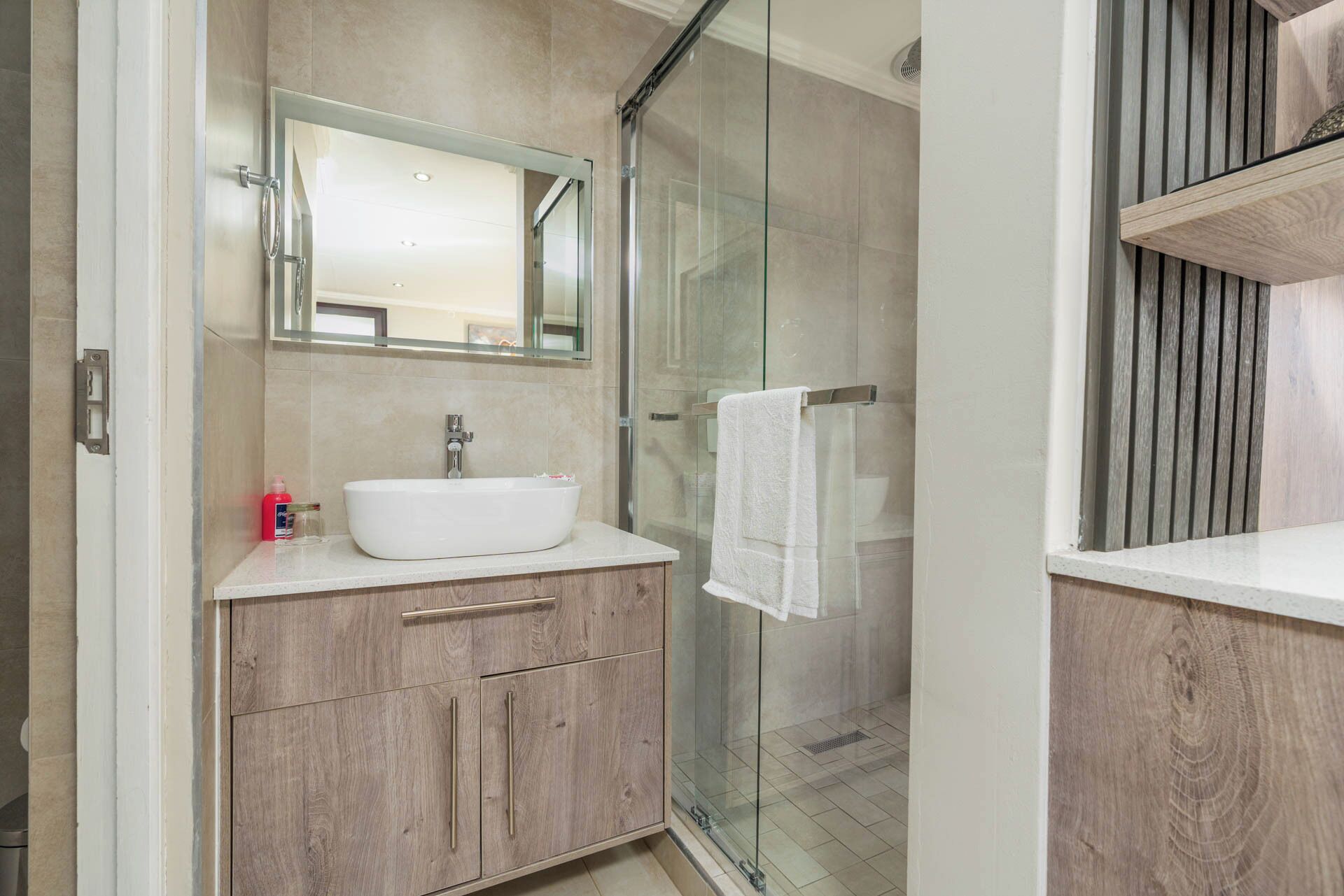 Un baño moderno con cabina de ducha de vidrio, un lavamanos blanco y armarios de madera.