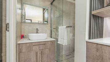 Un baño moderno con cabina de ducha de vidrio, un lavamanos blanco y armarios de madera.