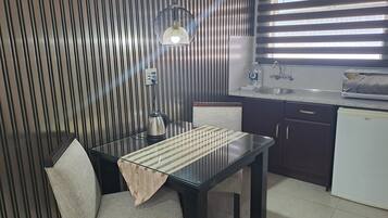 A compact kitchen with a dining table, chairs, a kettle, and a refrigerator.