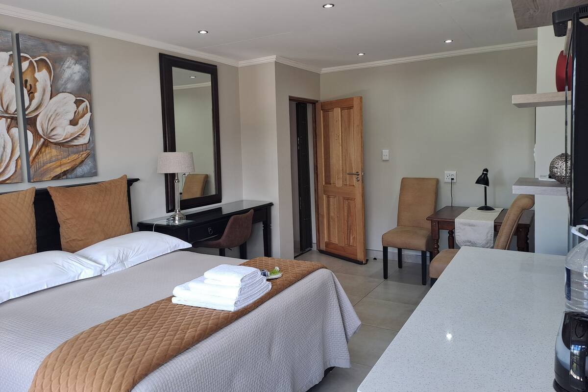 A hotel room with a bed, a desk, a chair, a table, and a large mirror.
