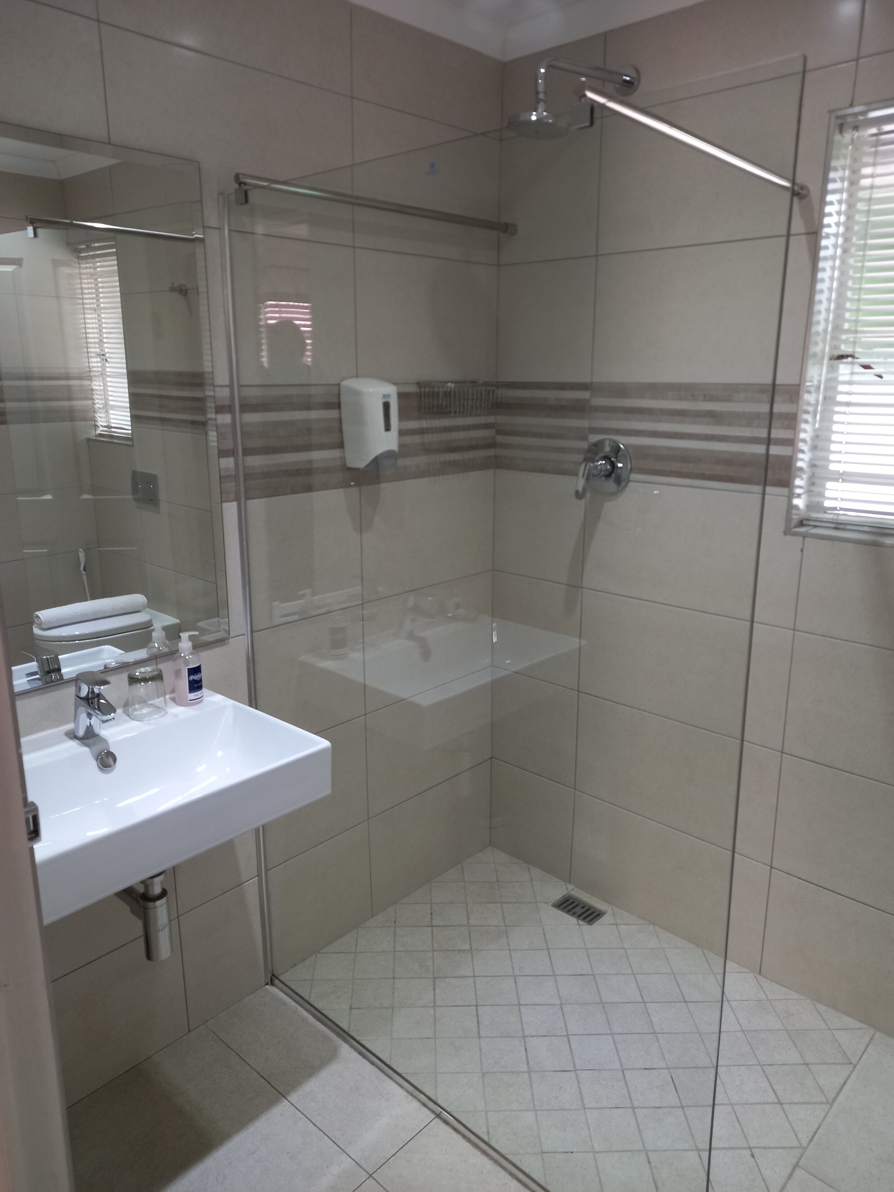 A bathroom with a glass-enclosed shower, a sink with toiletries, and a mirror.