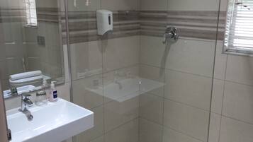 A bathroom with a glass-enclosed shower, a sink with toiletries, and a mirror.