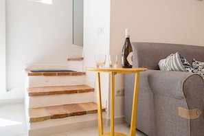 A staircase with a wooden finish, a grey sofa with patterned cushions, and a small round table with a bottle and glasses.