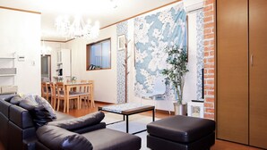 A modern living room with a sofa, ottoman, and a dining area with chairs and a table. - JL Guest House Daikokucho (Osaka)
