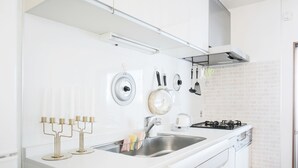 A modern kitchen with white cabinets, a stainless steel sink, and a gas stove. - JL Guest House Daikokucho (Osaka)