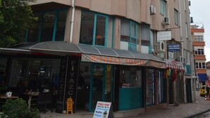 Ein mehrstöckiges Gebäude mit einem Café im Erdgeschoss namens „PIYAZCI YUSUF“ und einem Schild, das „Piyaz Çevrecilik“ bewirbt.