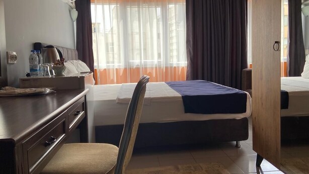 Ein Hotelzimmer mit einem Bett, einem Schreibtisch mit Telefon, einem Sessel und einem Fenster mit Vorhängen.
