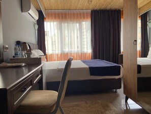 Een hotelkamer met een bed, een bureau met telefoon, een stoel en een raam met gordijnen.