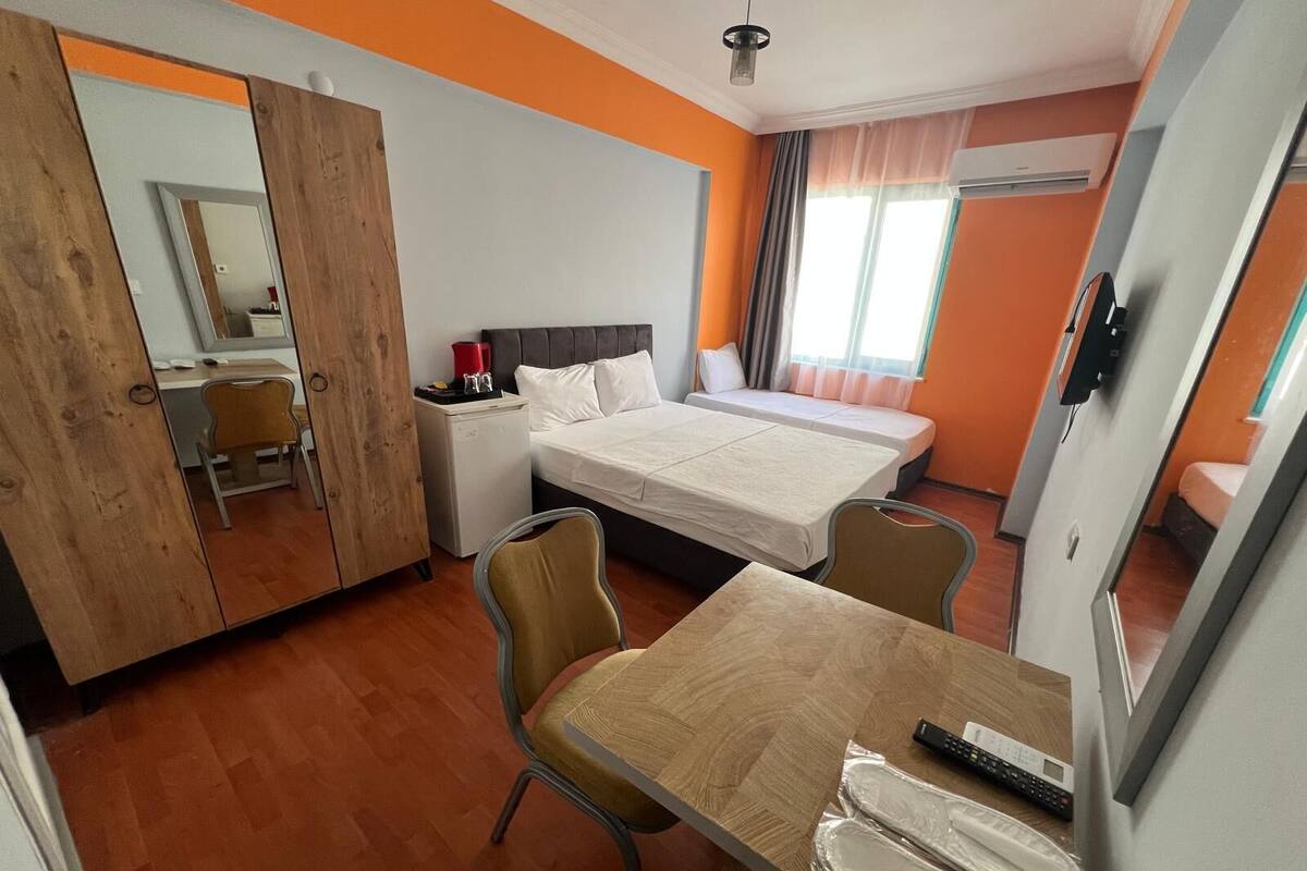 A hotel room with a bed, a desk, a chair, a small refrigerator, and a window with curtains.