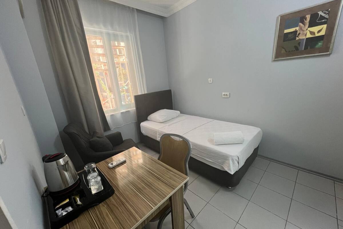 A hotel room with a bed, a desk with a coffee maker, a chair, and a window with curtains.